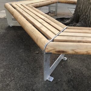 Banc tour d'arbre bois / métal. Banc en bois et en métal parfait pour une cour d’école. Son envergure permet l'installation autour d'un arbre de belle circonférence (sur la photo l'arbre fait 0,90 cm de diamètre). Le banc est conçu avec des angles arrondis pour plus de sécurité et de confort. Son bois chaleureux et ses solides profils en acier de 8 mm offrent au banc une robustesse à tout épreuve. Son design ludique et épuré s’accompagne d’une finition galvanisée pour une allure contemporaine, complétée éventuellement d’une peinture poudre pour une allure plus fun et ludique. Livré en 3 côtés montés (avec rondins et lattes des 3 autres côtés en attente) pour installation sur place.